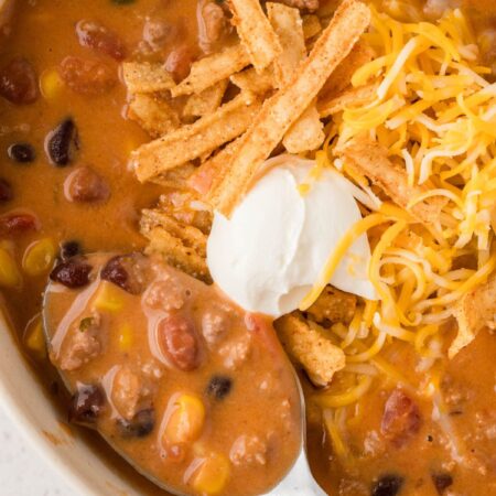 A bowl of taco soup with a spoon inside of it and with toppings.