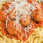 Bowl of pasta noodles with sauce and meatballs, and parmesan cheese.