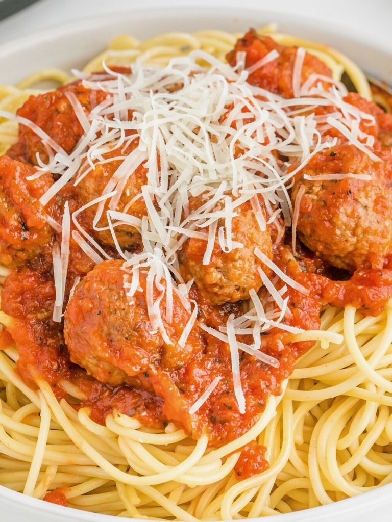 Bowl of pasta noodles with sauce and meatballs, and parmesan cheese. 