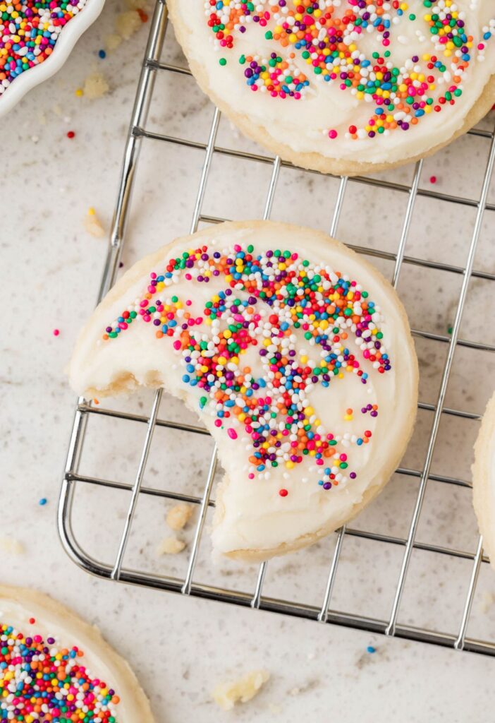 A cooling rack with a cookie on it with a bite taken out of it. 