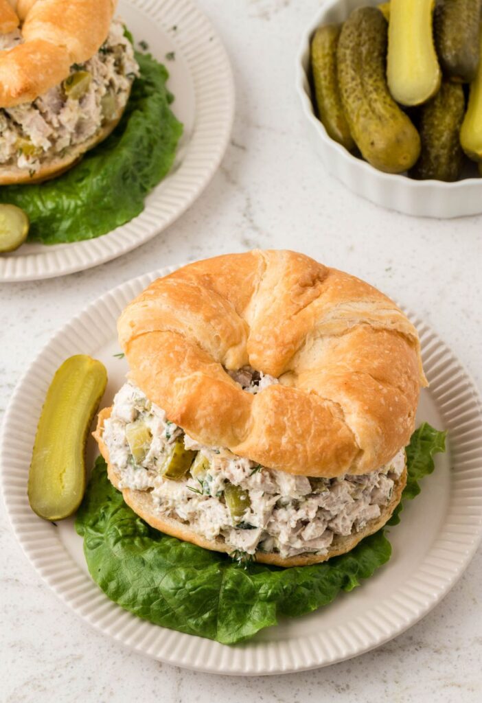 Overhead pic of a chicken salad sandwich with a bowl of pickles. 