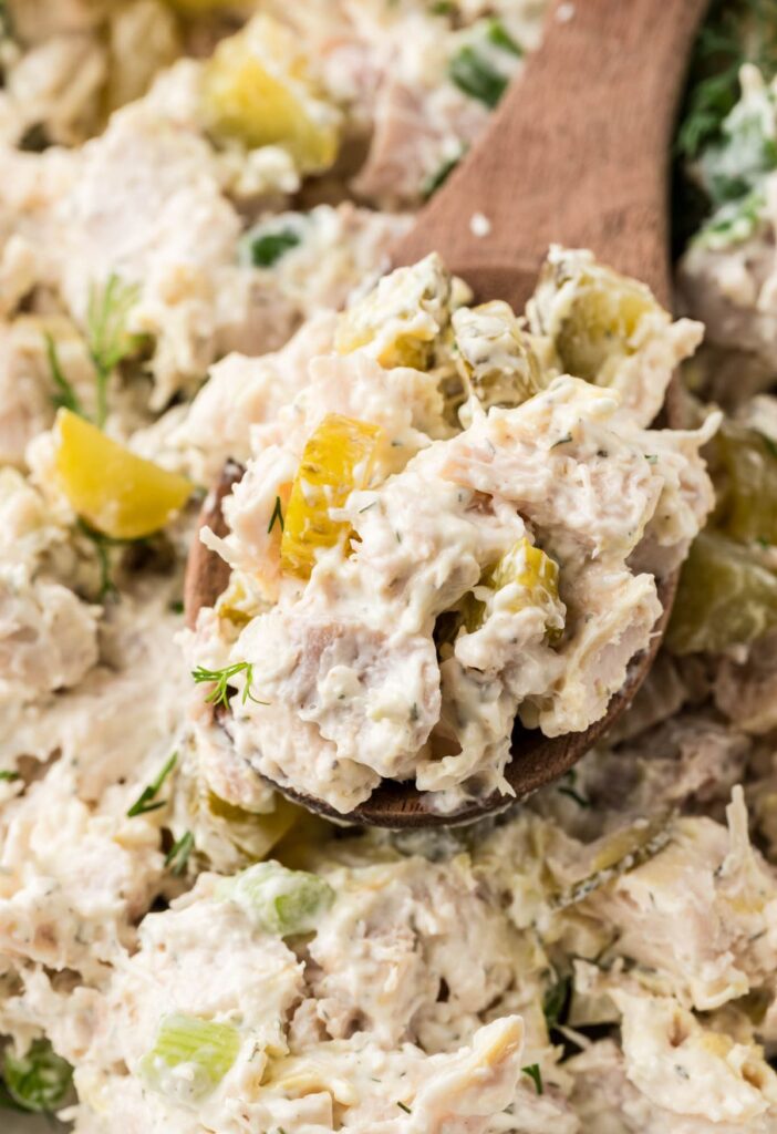 The chicken salad with a wooden spoon taking a scoop of it. 