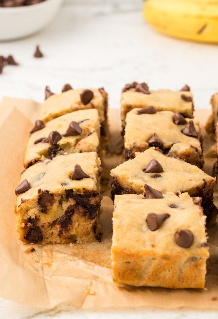 Banana bars on parchment paper with a fresh banana in the background.