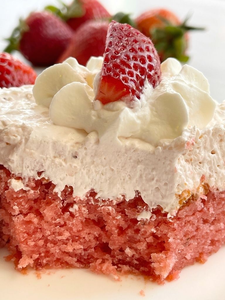 Strawberry cake on a plate with a bite taken out of it to show the moist texture of the cake.
