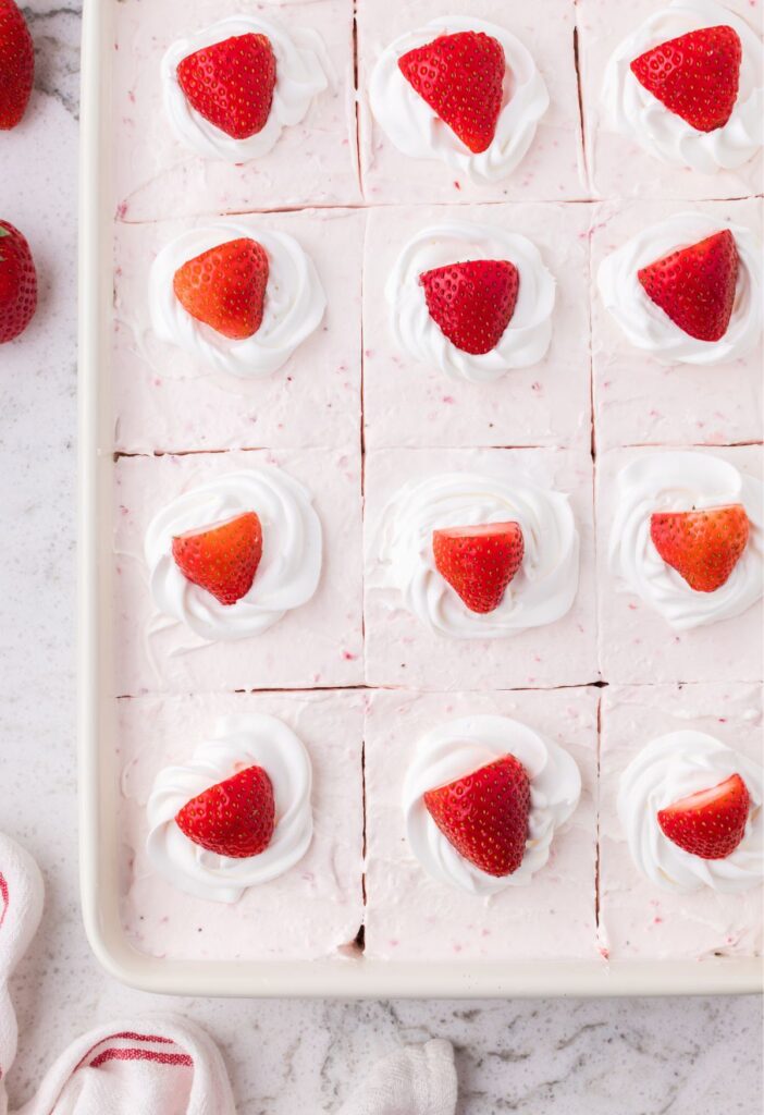 Pan of the strawberry cake with a red cloth and bowl of strawberries in the background. 