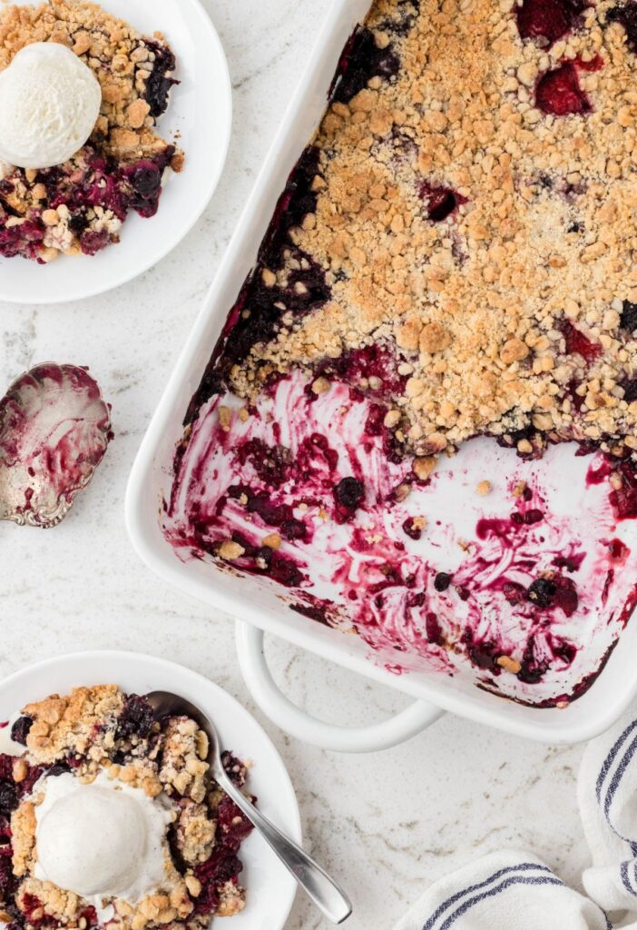 Overhead pic of the pan of berry crisp with a plate with a serving on it with ice cream. 