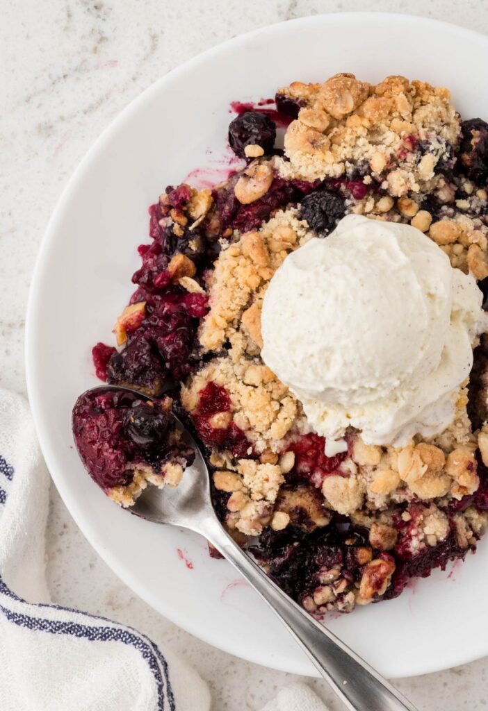 Picture of a plate of the berry crisp dessert with a spoon on it. 