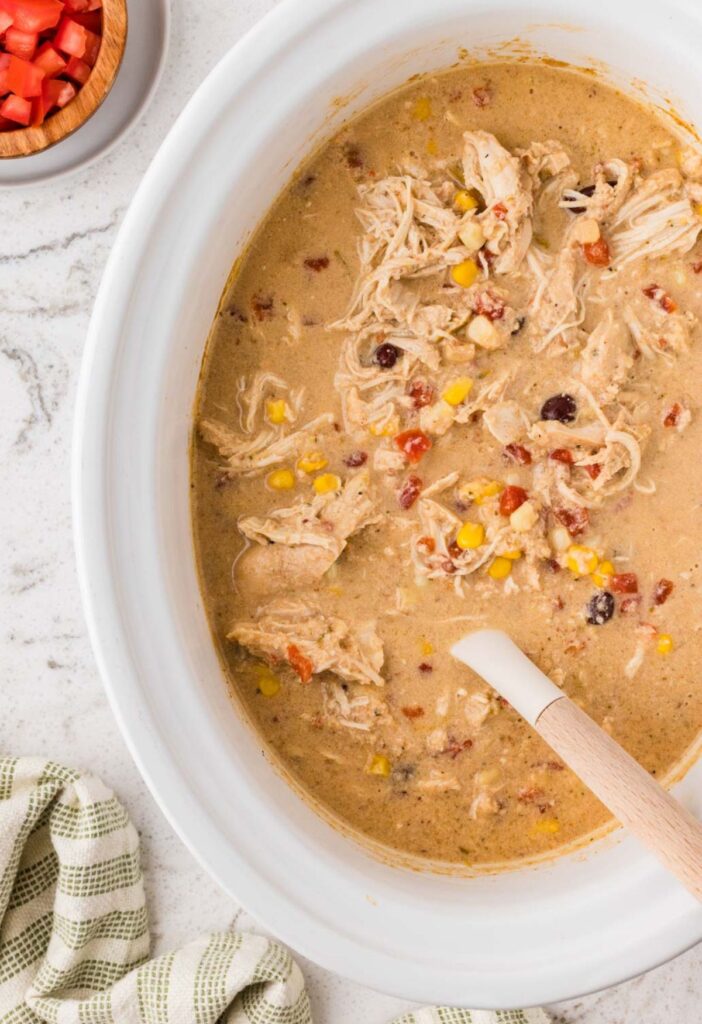 The white slow cooker with the cream chicken mixture, a serving spoon, and a side of rice.