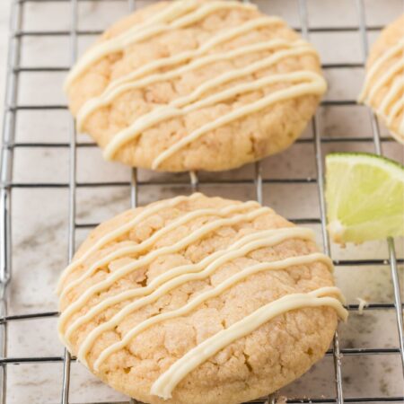 A wire rack with the baked key lime cookies on them and lime wedges.