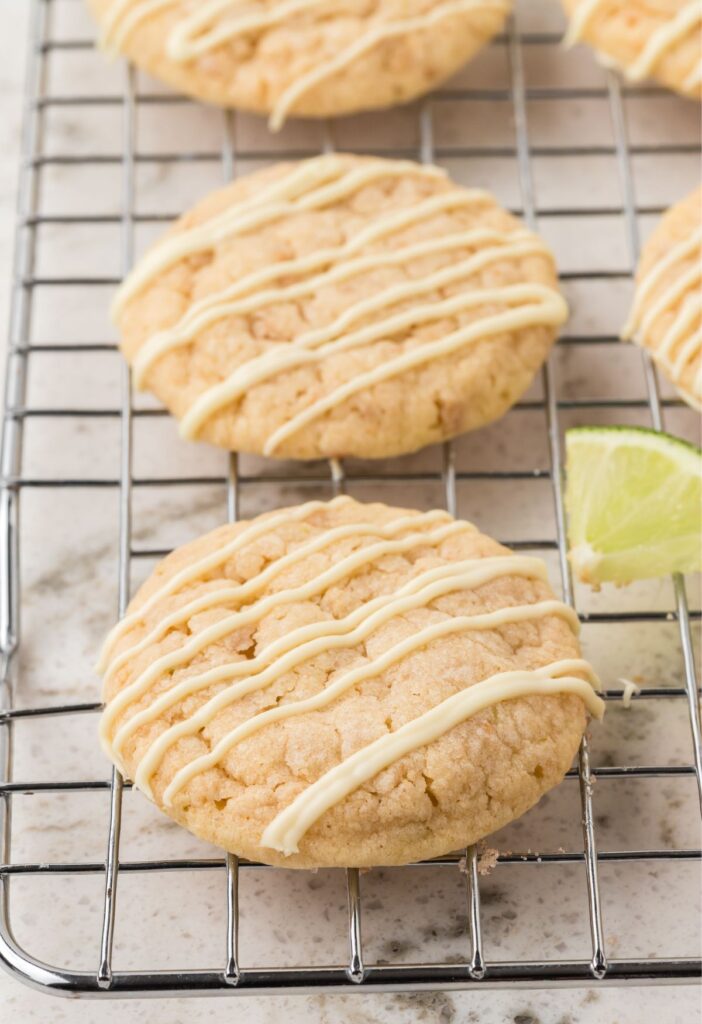 A wire rack with the baked key lime cookies on them and lime wedges.