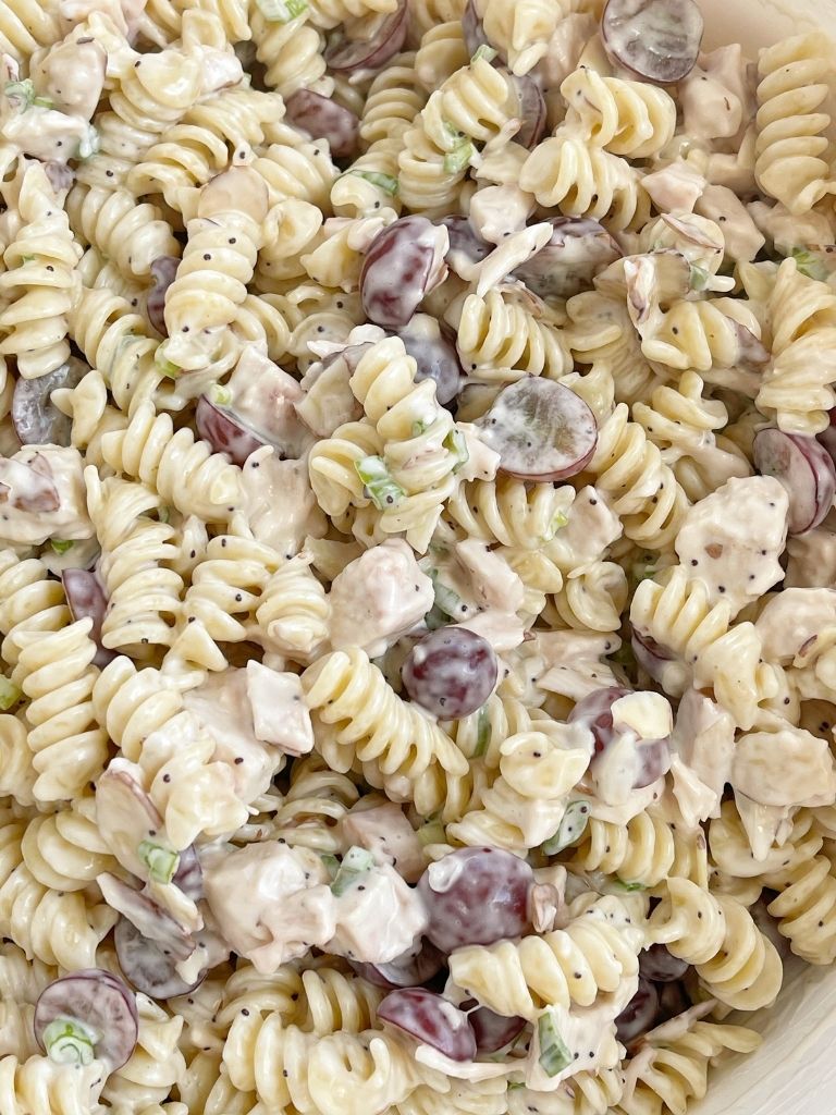 A bowl of pasta salad with chicken, grapes, poppy seeds, and almonds. 