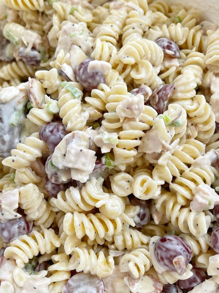 Poppy seed pasta salad inside a bowl with a wooden spoon. 