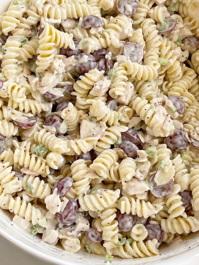 A bowl with chicken pasta salad in it, with grapes, almonds, and poppyseed dressing. 