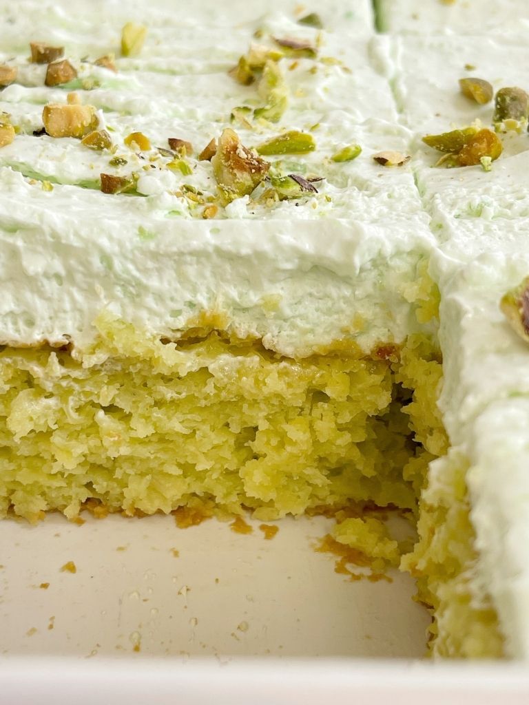 Pistachio cake inside a white pan topped with pistachio pudding frosting. 