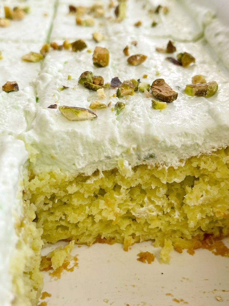 Cake inside a white pan topped with frosting and pistachios.