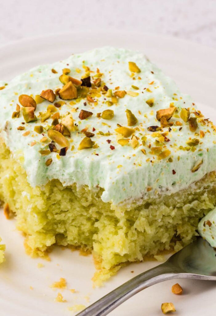 A piece of pineapple cake with frosting, with a fork bite taken out of the center of the piece.