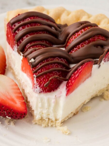 A slice of cream pie with strawberries on top and a chocolate drizzle