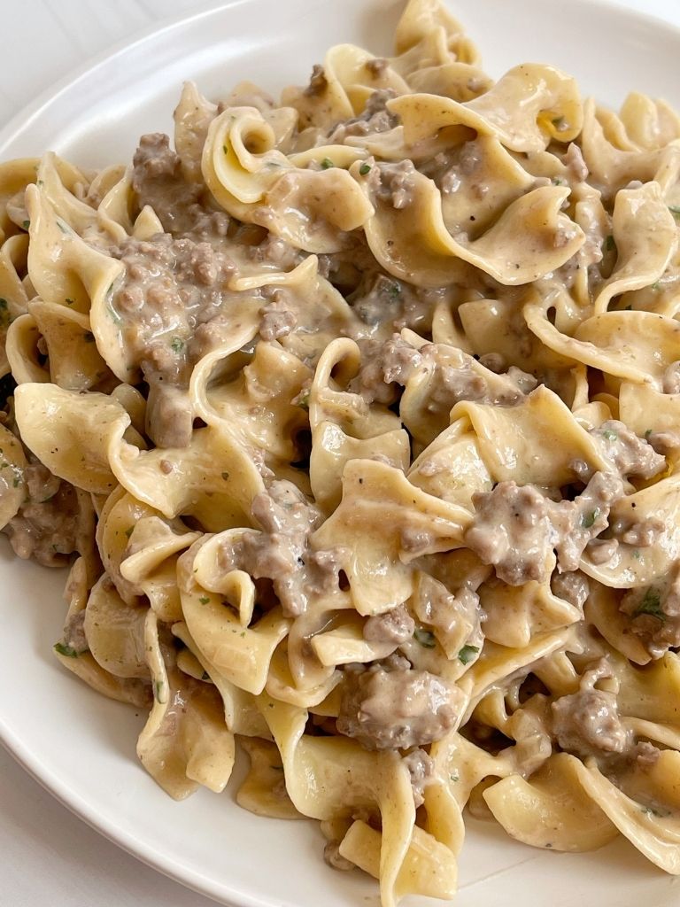 A white plate with beef stroganoff and egg noodles on it. 
