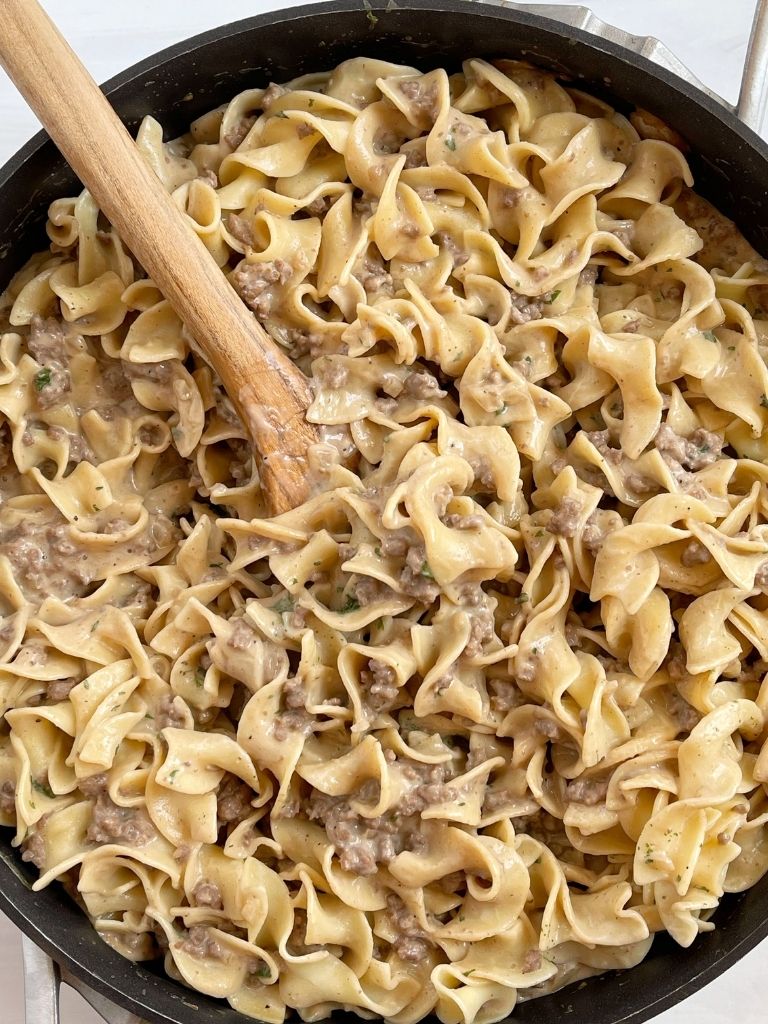 A skillet pan with beef stroganoff and a wooden spoon in it. 