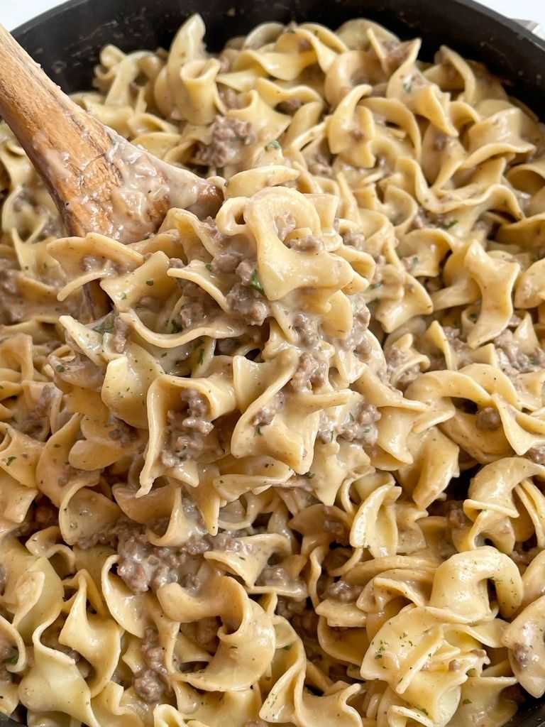 A scoop of beef stroganoff on a wooden spoon inside a skillet pan.