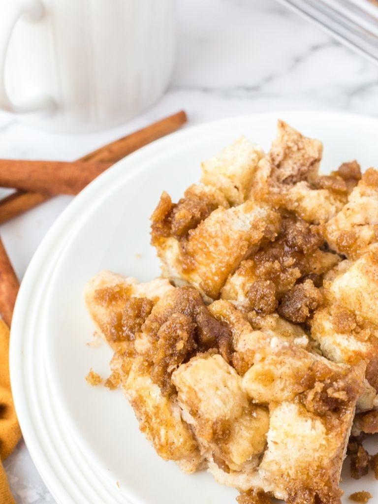 Picture of French toast casserole on a white plate with cinnamon sticks in the background.