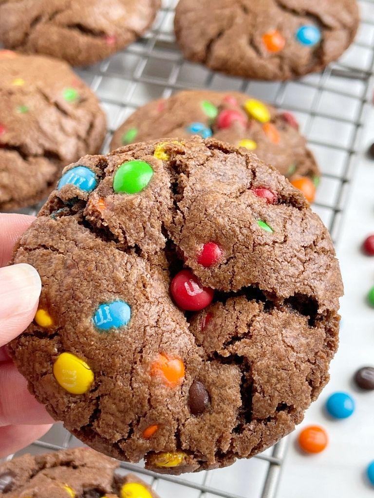 A picture of a hand holding a chocolate cookie with m&m on top and inside the cookie. 