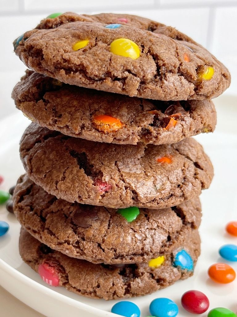 A stack of chocolate m&m cookies on a white plate.
