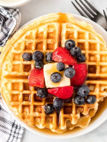 Hero shot of a stack of waffles topped with syrup, butter, and fruit.