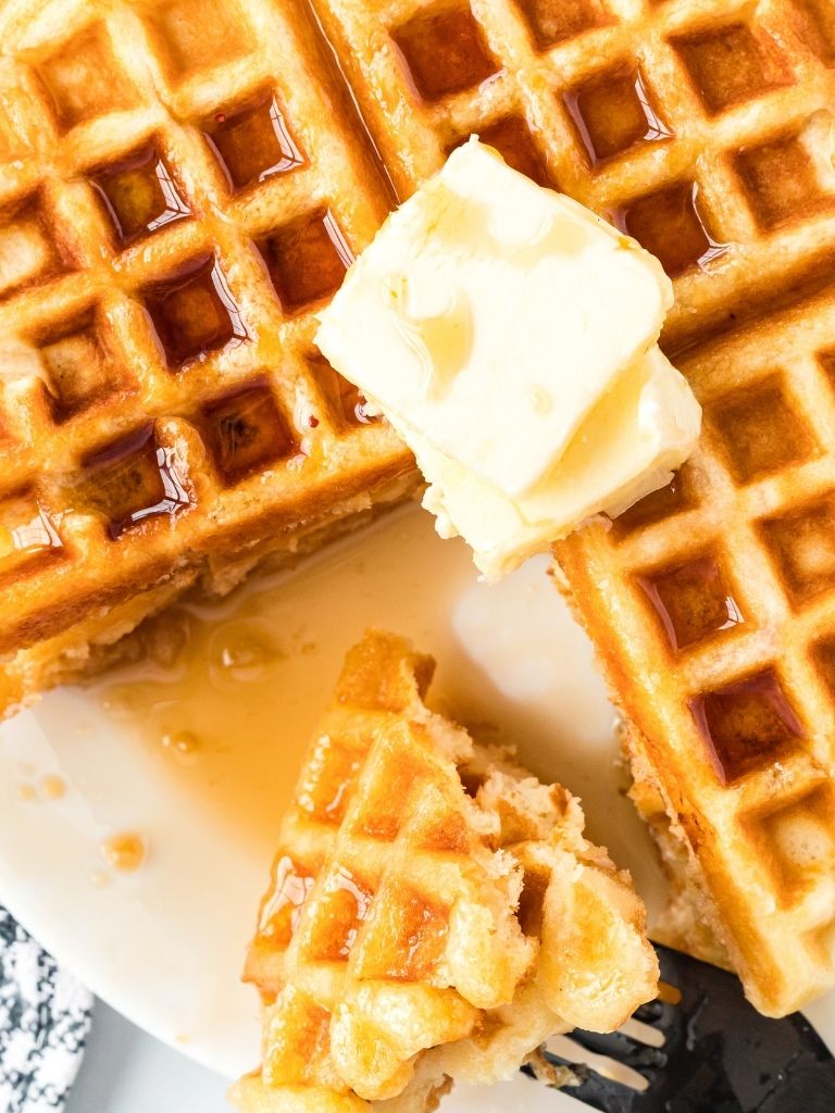 Close up shot of waffles with a fork holding some and topped with butter and syrup.