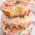 Stack of donuts made with a cake mix and topped with glaze and sprinkles on white plate.