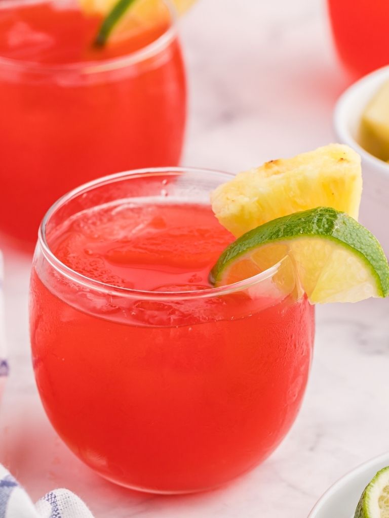 Two cups of punch garnished with lime and pineapple. 