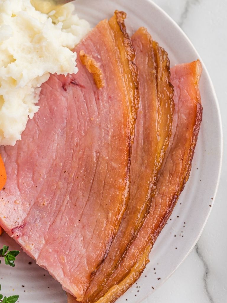 Slices of ham on a white plate with mashed potatoes. 