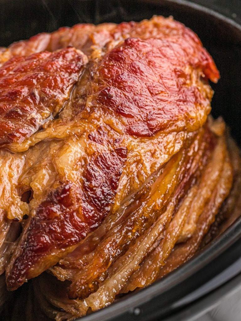 Slow cooker with a ham inside of it showing the spiral cuts and brown sugar crust. 