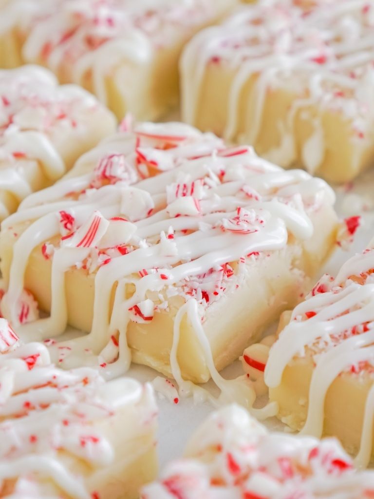 White chocolate fudge topped with peppermint pieces and a chocolate drizzle on a white background. 