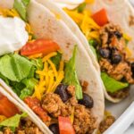 Ground turkey tacos inside soft tortillas on a white plate with toppings.