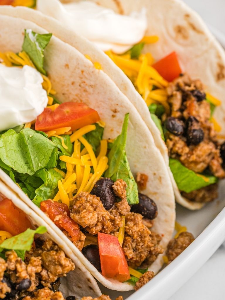 Ground turkey tacos inside soft tortillas on a white plate with toppings.
