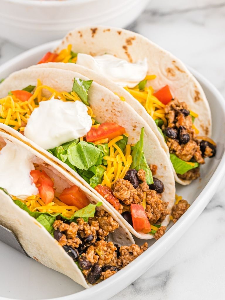 Platter of soft tortillas filled with ground turkey taco meat and topped with sour cream, cheese, lettuce, and tomatoes. 