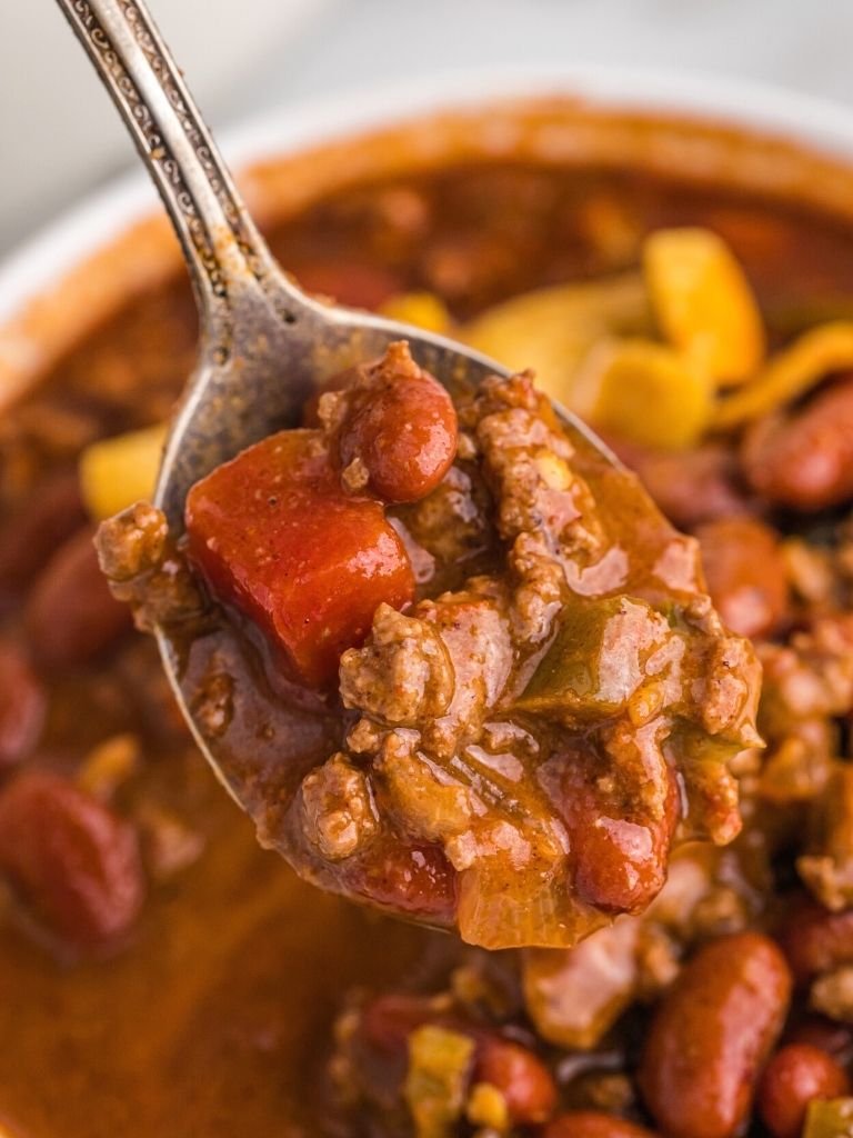 Spoonful of chili with a white bowl of chili in the background. 