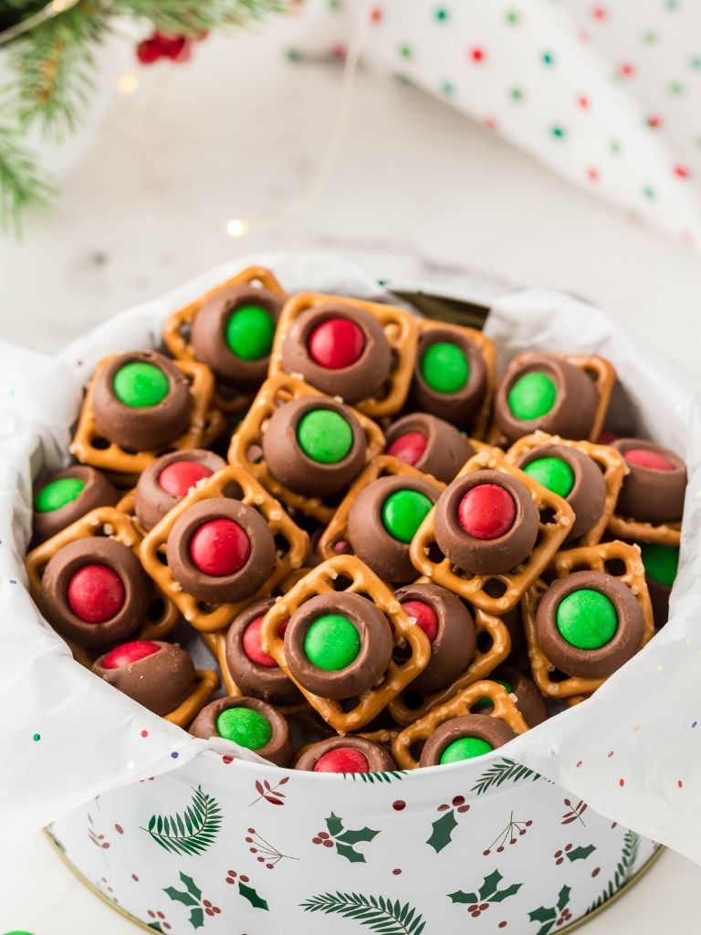 A tin of rolo pretzels with Christmas background.