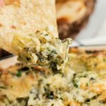 A tortilla chip dipped inside a baking dish with artichoke spinach dip.