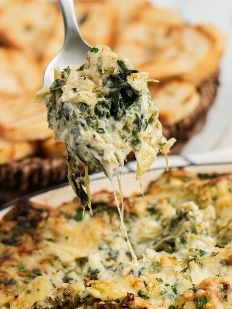 A spoonful of artichoke dip on a spoon with the dip in the background. 