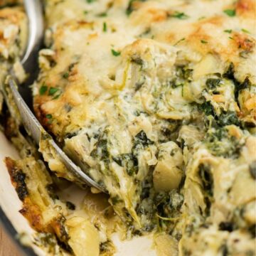 A dish of hot baked spinach artichoke dip with a spoon inside of it.