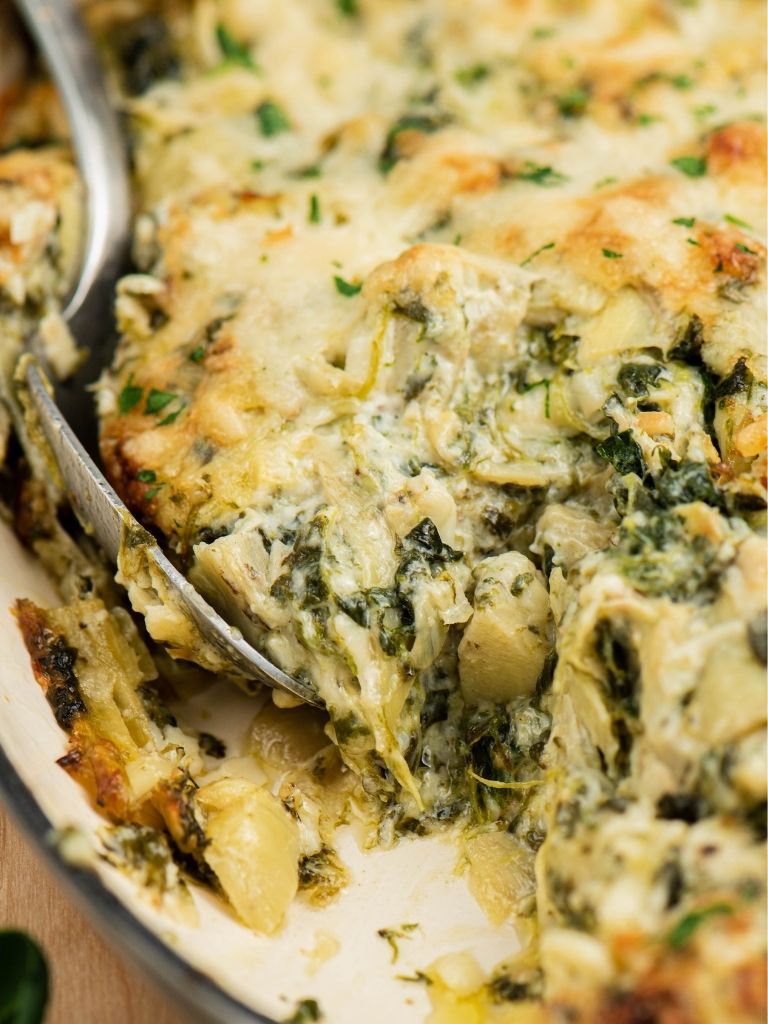 A dish of hot baked spinach artichoke dip with a spoon inside of it. 