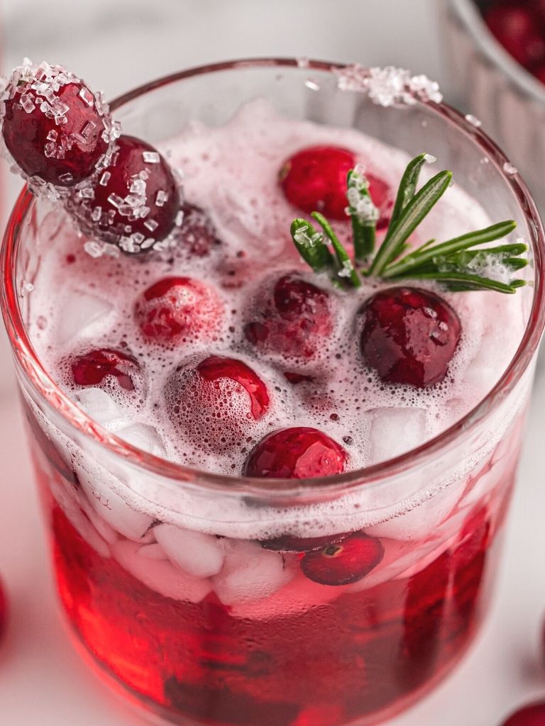 A glass cup with cranberry cider punch with ice cubes, sugared cranberries, and sage for decoration. 