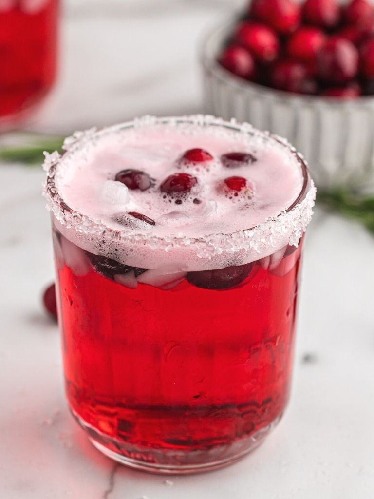 Cup of cranberry punch topped with fresh cranberries.