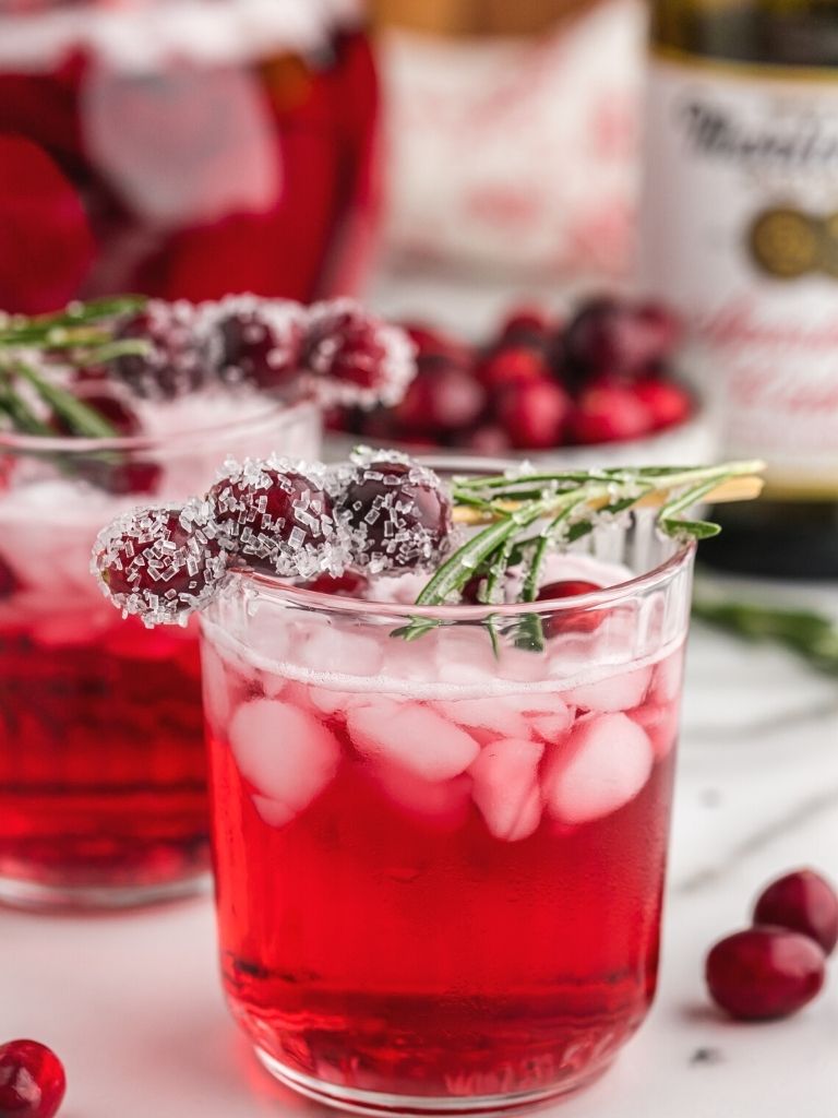 Cranberry punch in a glass cup with ice and decorate cranberries and rosemary on top.