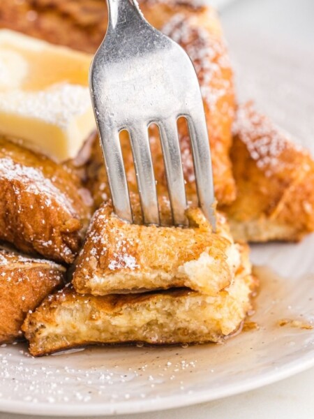 A plate with French toast with syrup and a fork pushing into some of it.
