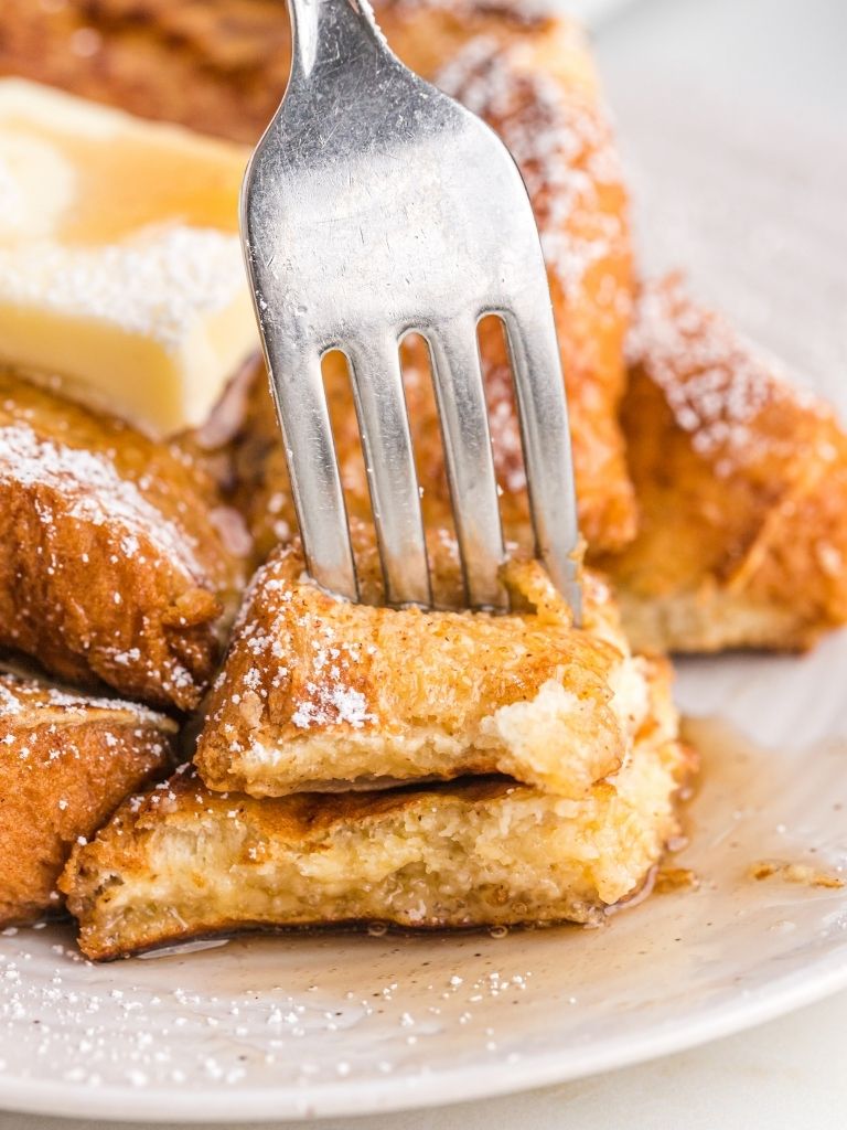 A plate with French toast with syrup and a fork pushing into some of it. 