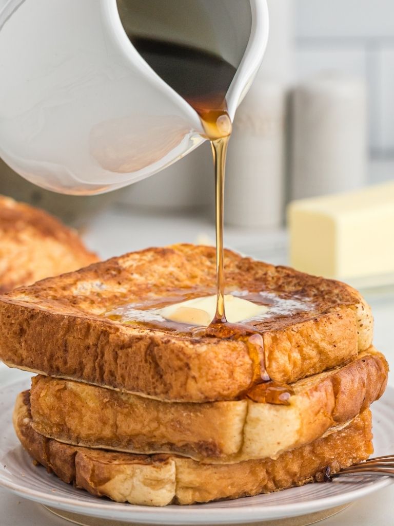 Stack of French toast with butter on top. Motion picture of syrup being poured over the stack. 