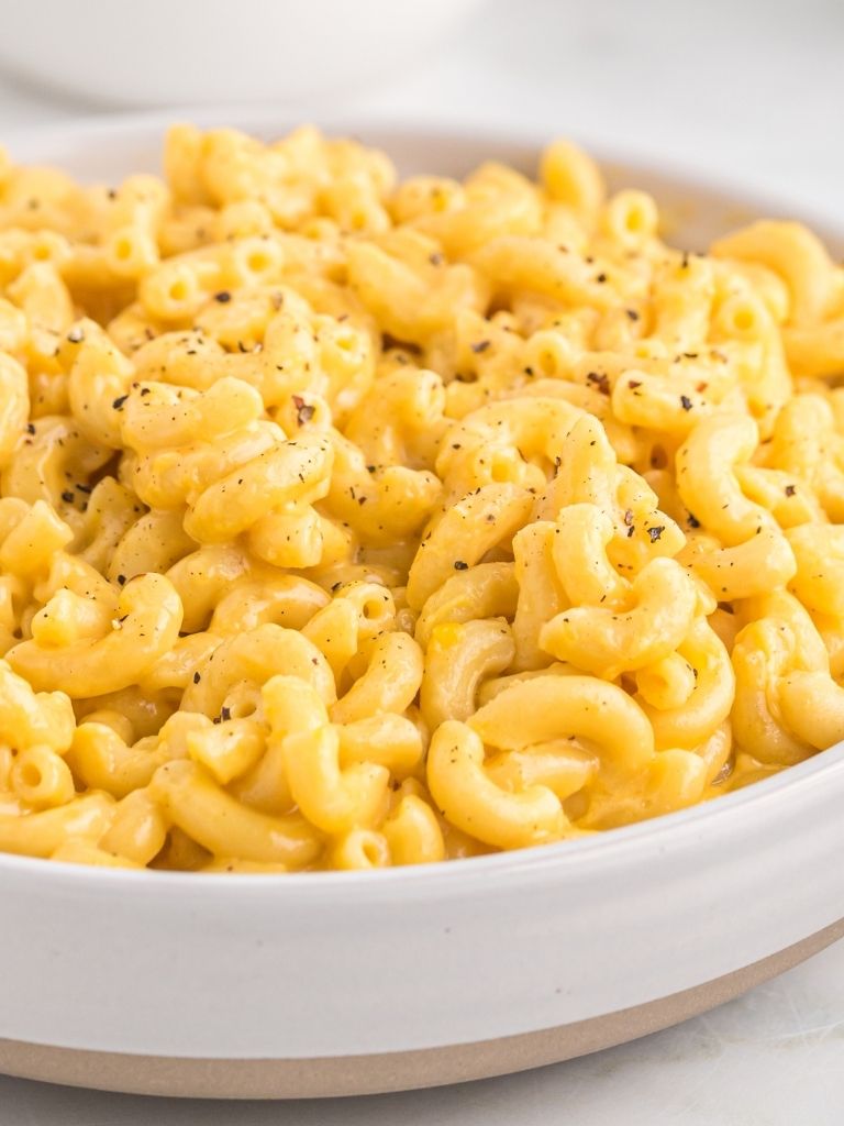 A white and tan serving bowl full of macaroni and cheese topped with pepper for garnish.